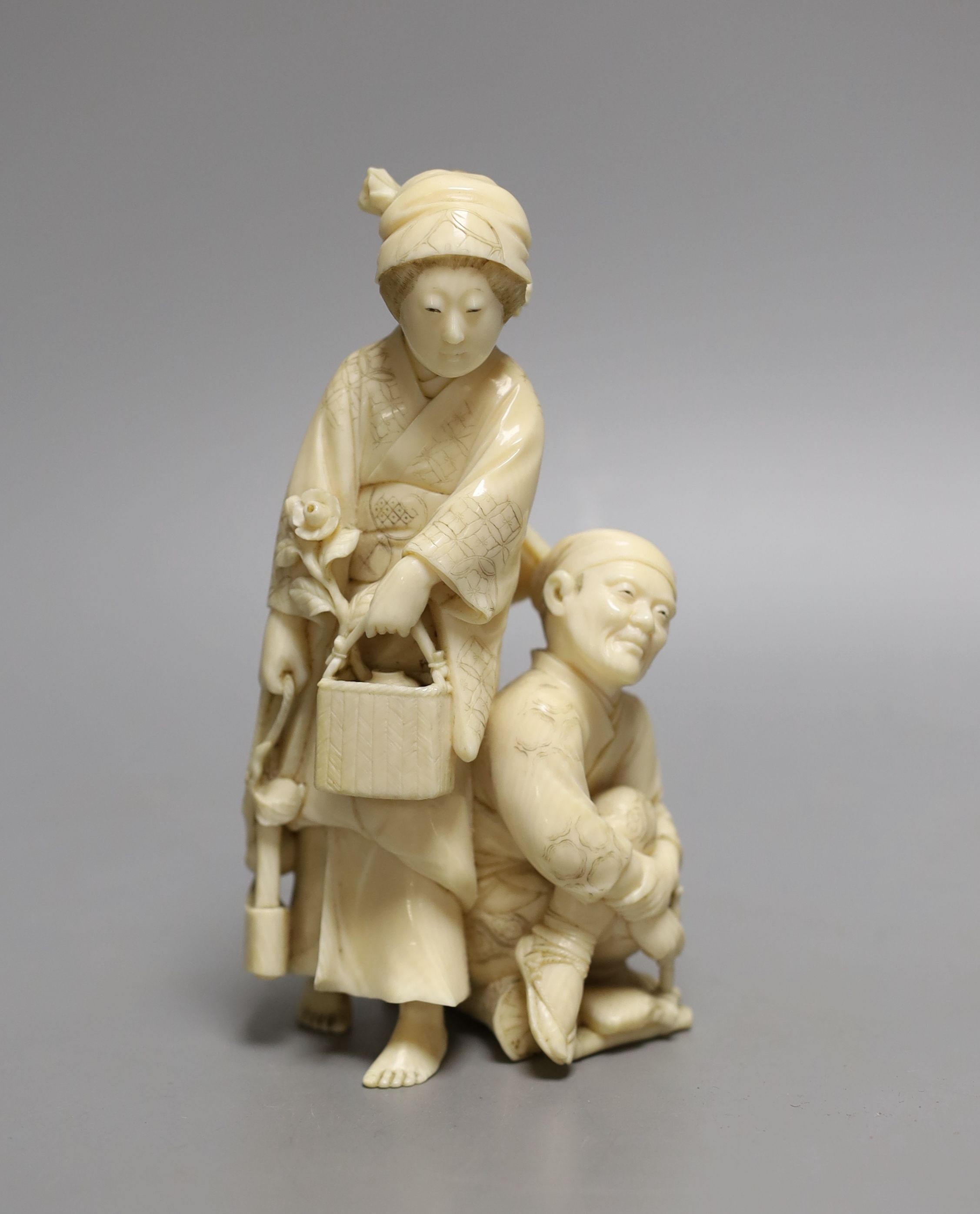 A Japanese ivory okimono of a crouching man and a woman holding a flower basket, Meiji period, signed - 15cm tall